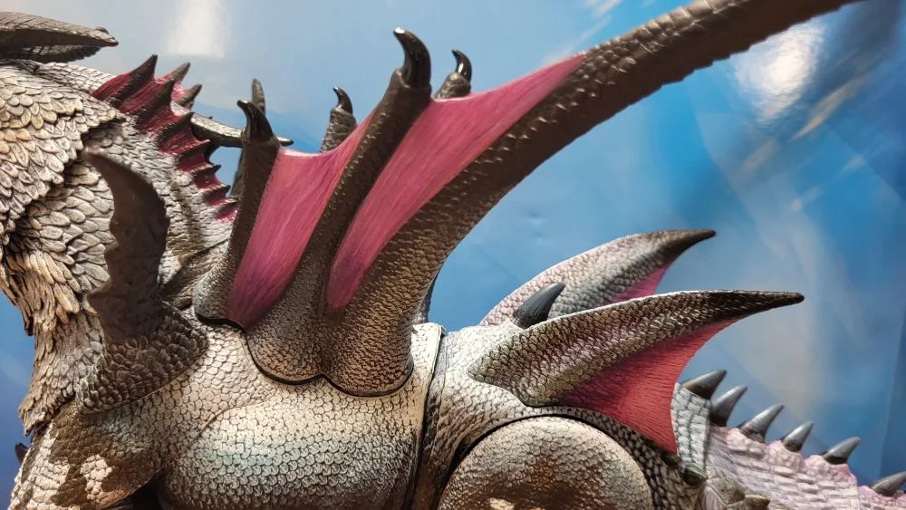 A close up of the figure's wings from the left side view. Figure is in front of the included package backdrop.