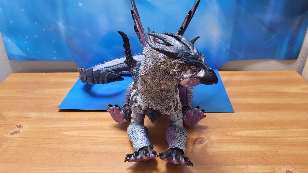 Figure is in a sitting posture. Front view this time. Neck is posed up, and slightly to the left. Jaw is closed. Tail is curled on the right as much as possible. Figure is in front of the included package backdrop.