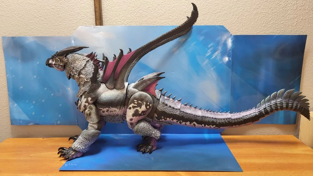 A complete left side view of the figure. Figure is in front of the included package backdrop. Jaw is closed. Tail is straightened out.