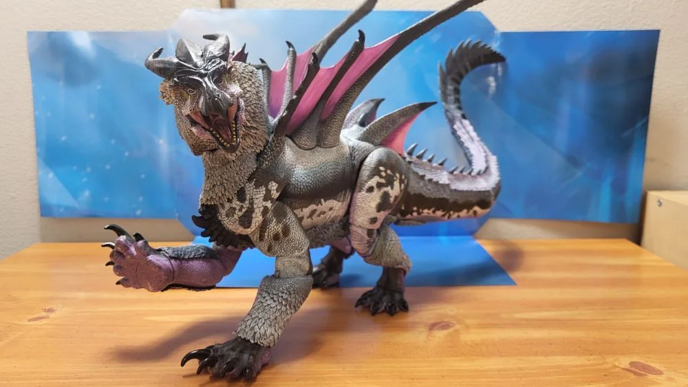 An attempt at recreating the pose in the concept art done by Felipe Massafera, but from another angle. The figure is mostly shown from the left side, with the head turned to face the camera. Jaw is open, right fore paw is raised. Figure is in front of the included package backdrop.