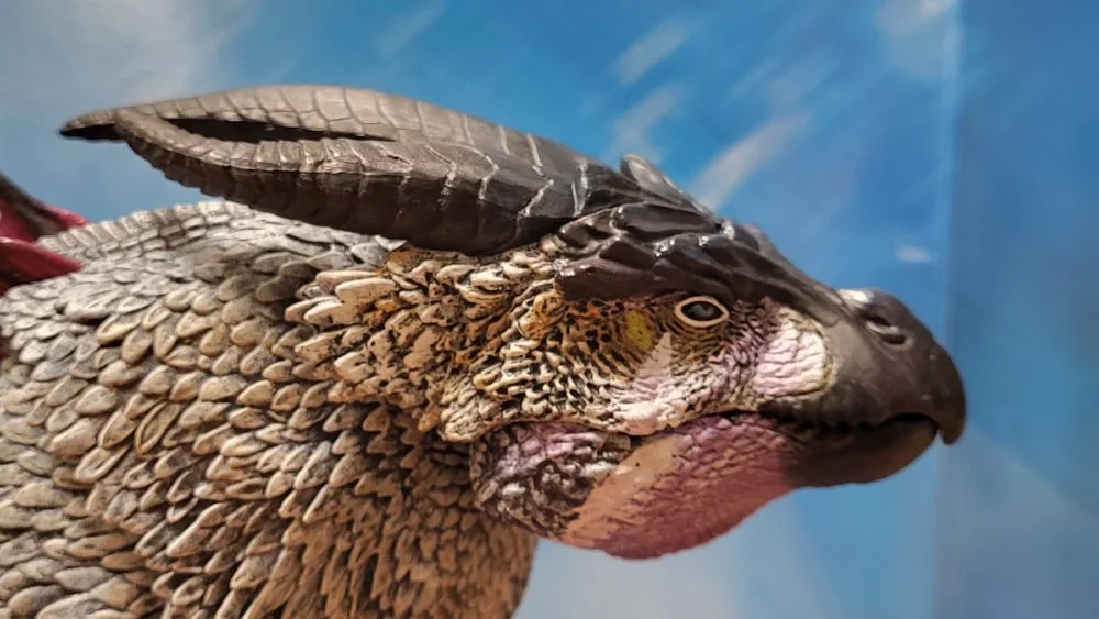 A close up of the figure's head from the right side view. Figure is in front of the included package backdrop. Jaw is closed.