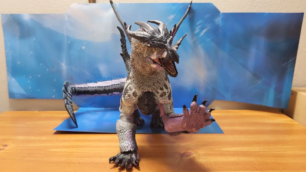 A front side view of the figure. Head is turned to the right, jaw is open. Left fore paw is raised. Figure is in front of the included package backdrop.