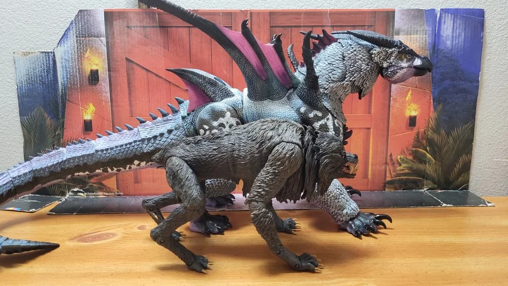 Comparison with the NECA Ultimate Kessler Wolf. Both figures from a right side view. The werewolf is in front of Kuraokami.. Both in a neutral pose with jaws closed. In front of the reviewer's typical JW background.