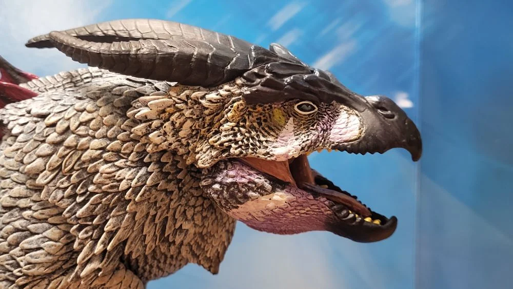 A close up of the figure's head from the right side view. Figure is in front of the included package backdrop. Jaw is opened.