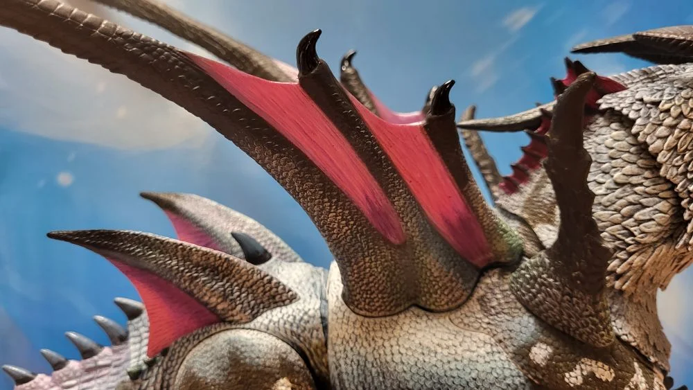 A close up of the figure's wings from the right side view. Figure is in front of the included package backdrop.
