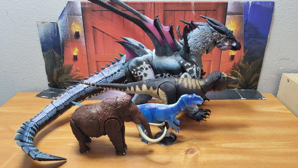 Figures in a right side view. All in a neutral pose with jaws closed. Kurokami is in the back, with the T. rex in front of it. The Allosaurus is in front of the T. rex, and the mammoth is in front of the Allosaurus, but also placed behind it. All are in front of the reviewer's typical JW background.